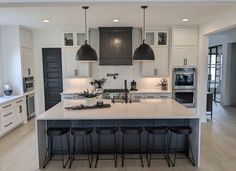 a large kitchen with an island and bar stools in the center, surrounded by white cabinets