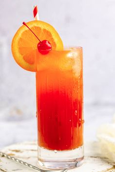 an orange drink with a cherry garnish on the rim and a straw in it