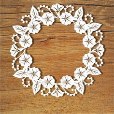 a white paper wreath with flowers and leaves on a wooden surface, ready to be cut out