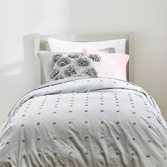 a bed with grey and pink pillows on top of it next to a white headboard