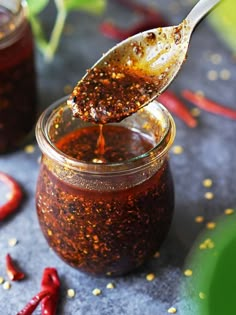 a spoon full of chili sauce on top of a table with red peppers around it