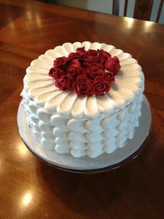 a white cake topped with red roses on top of a wooden table