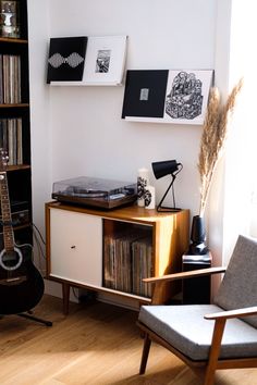 a record player is sitting on top of a cabinet next to a chair and bookshelf