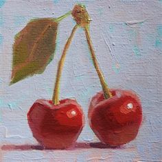 two cherries on a white surface with a green leaf