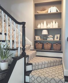 the stairs are lined with baskets, vases and pictures on shelves in this entryway