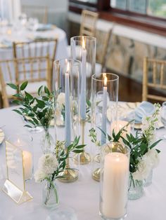 the table is set with candles, flowers and greenery in glass vases for centerpieces