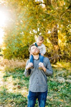 a man holding a small child in his arms while standing in the grass with trees behind him