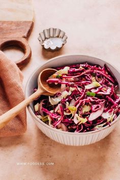 a white bowl filled with red cabbage salad next to a wooden spoon on a table