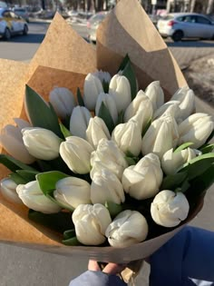 a person holding a bouquet of white tulips in their hand on the street