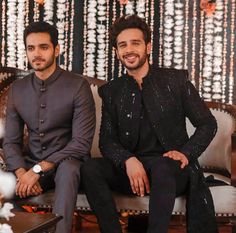 two men sitting on top of a couch in front of a wall covered with beads