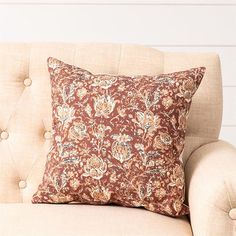 a brown and white pillow sitting on top of a beige couch next to a wall