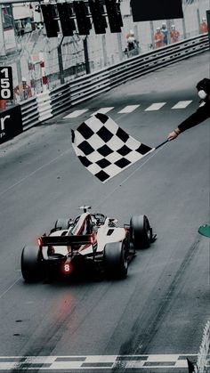 a man holding a checkered flag next to a racing car on a race track