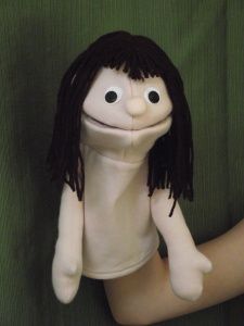 a stuffed doll with long hair and black eyes sitting on a green clothed surface