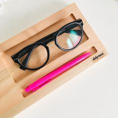 a pair of black glasses sitting on top of a wooden box next to a pink pen