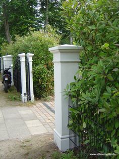 a white fence and gate in the middle of a sidewalk with trees on both sides