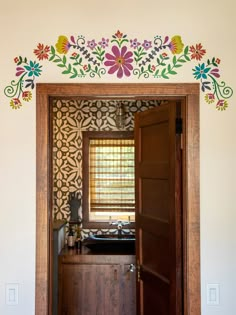 an open door leading to a kitchen with flowers painted on the wall and wooden cabinets