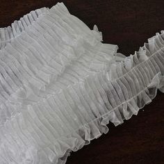 a piece of white cloth with ruffles on it sitting on a wooden surface