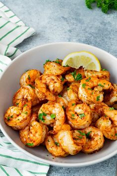 a white bowl filled with cooked shrimp and garnished with parsley next to a lemon wedge