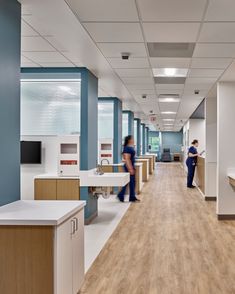 two people are walking down the long hallway in an office with blue and white walls