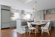 a kitchen with wooden floors and gray cabinets, two white chairs at the center of the table