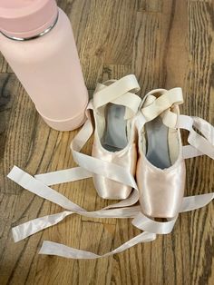 a pair of ballet shoes tied up on a wooden floor next to a water bottle