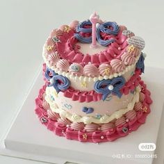 a three layer cake decorated with pink, blue and white icing on top of a box