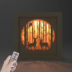 a hand holding a remote control in front of a shadow box with deer silhouettes