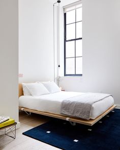 a bed sitting on top of a blue rug in a bedroom next to a window