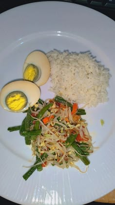 a white plate topped with rice, eggs and veggies next to an egg