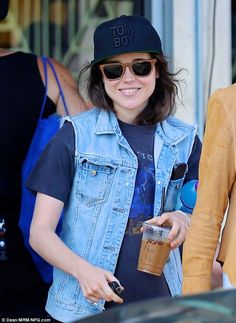 a woman wearing sunglasses and a denim vest is holding a coffee in her hand while walking down the street