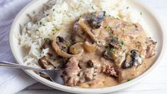 a white plate topped with rice and meat covered in mushroom gravy