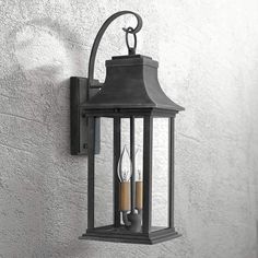 an outdoor wall light with two candles on the front and side of it, against a white stucco wall