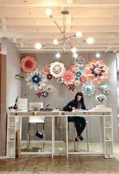 a woman sitting at a desk in front of paper flowers