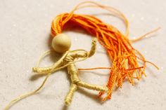 an orange and yellow piece of string with a wooden bead in the shape of a man