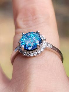 a close up of a person's hand holding a ring with a blue stone in it