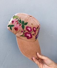 a person is holding up a baseball cap with flowers on the front and side, against a blue wall