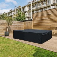 an outdoor patio with a black cover on the ground next to a wooden fence and building