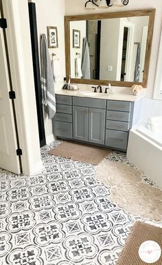 a bathroom with gray and white tiles on the floor, mirror above the bathtub