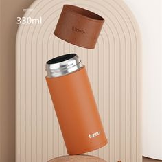 an orange coffee cup sitting on top of a wooden table next to a metal can