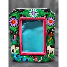 a colorful photo frame with flowers and people painted on the front, sitting on a table