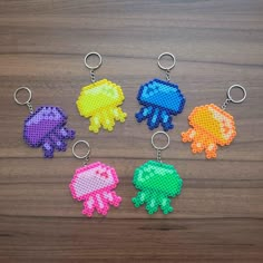 six perler keychains with different designs on them sitting on a wooden surface