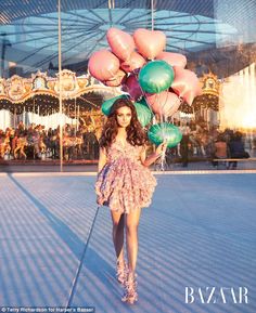 a woman is walking down the street with balloons on her head and in front of an amusement park