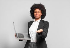 a woman holding a laptop computer in her right hand and pointing to the side with both hands