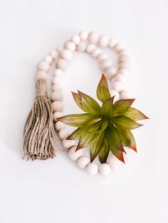 a white beaded bracelet with a green leaf and tassel