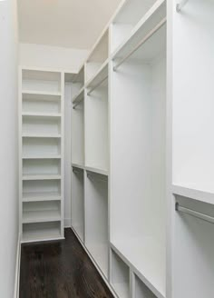 an empty walk in closet with white shelving and wood flooring on the side