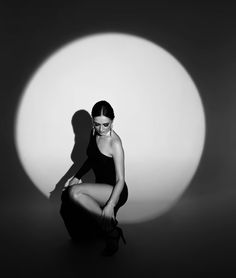 a woman kneeling down in front of a white ball with her shadow on the wall