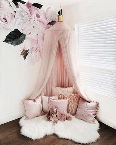 a canopy bed with pink pillows and flowers on the wall behind it, in front of a window