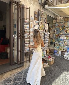 a woman in a white dress is looking at pictures on display outside a storefront