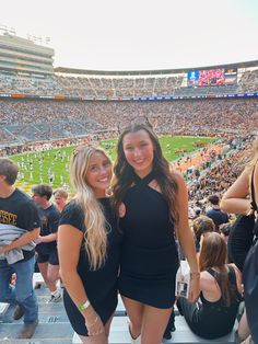 two beautiful young women standing next to each other in front of a stadium filled with people