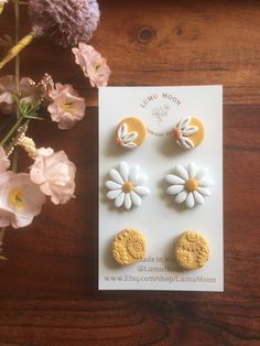 three yellow and white flower studs sitting on top of a card next to flowers